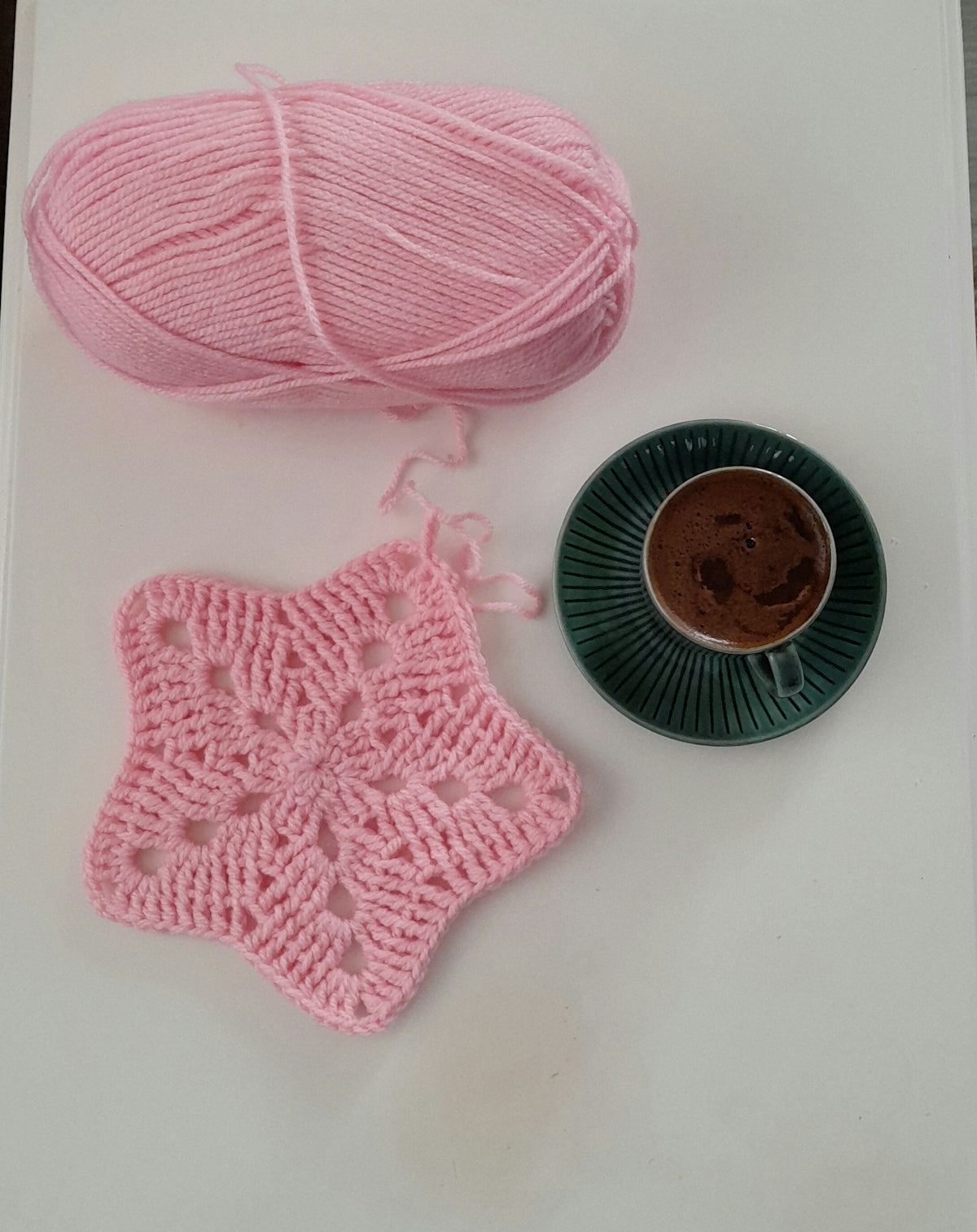 Pink yarn, star doily, and coffee cup on white surface