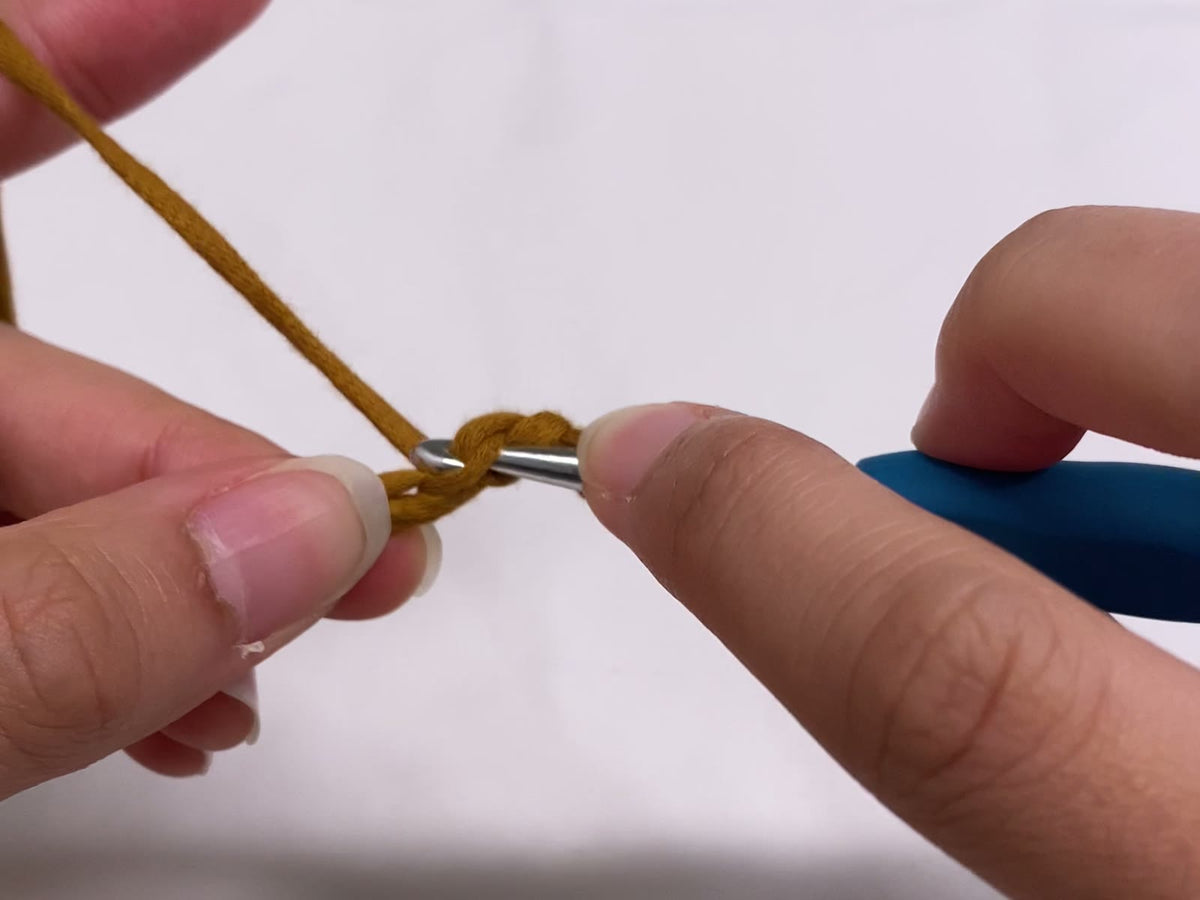 Crochet hook inserted into a short foundation chain of golden yarn, ready to work the first stitch