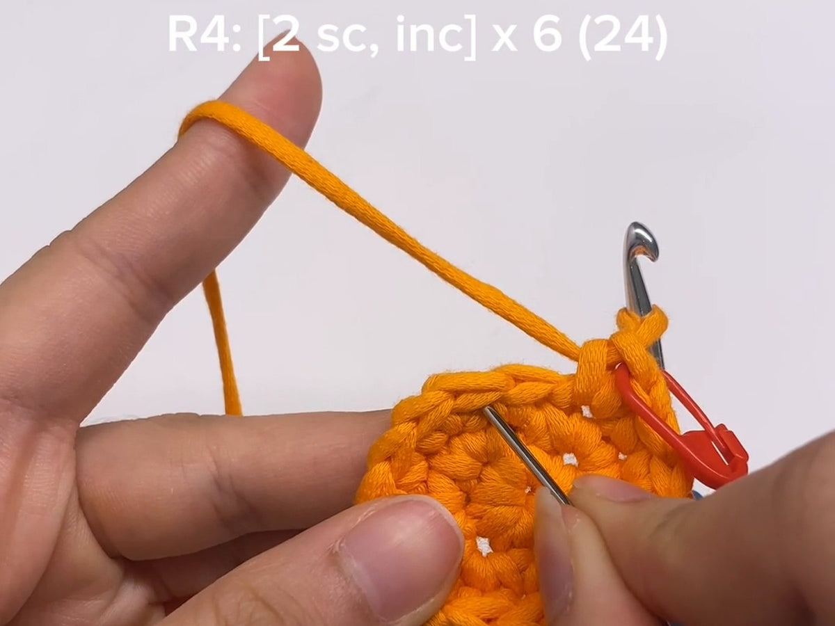 Pointing to the stitches of round 4 on an orange amigurumi circle, with the pattern line R4: [2 sc, inc] x 6 (24) shown above