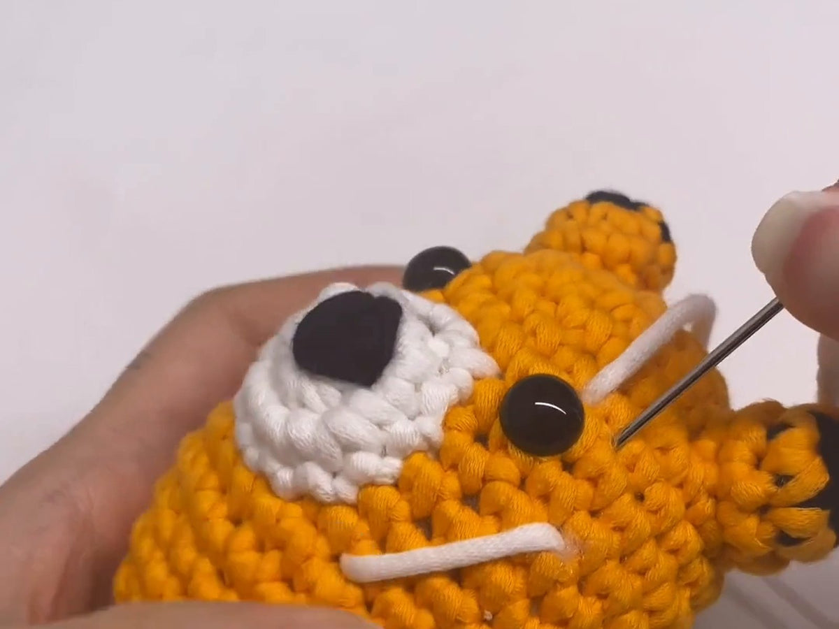 Embroidering the face markings on a crocheted red panda with a yarn needle