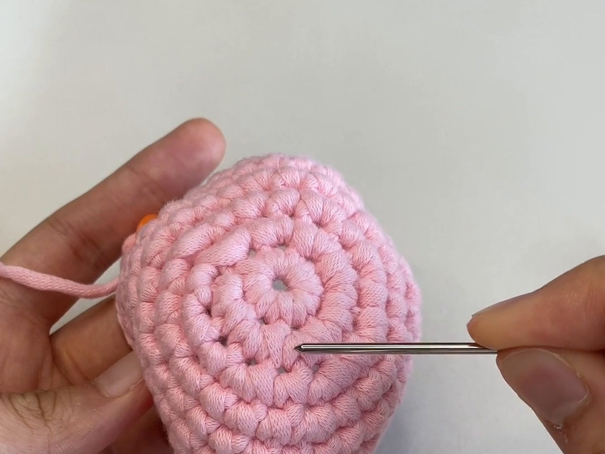 Checking a pink crochet piece round by round with a yarn needle