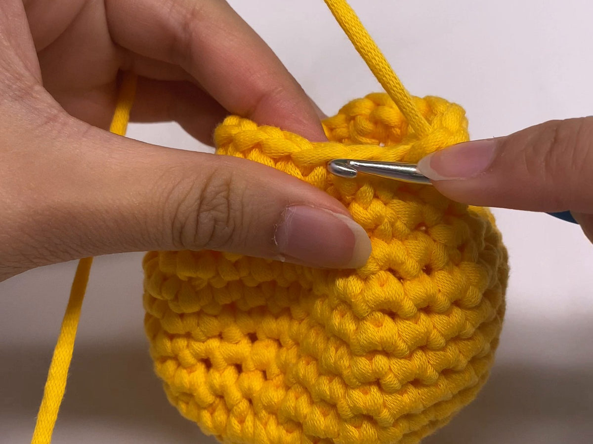 Crocheting a round in front loops only on a yellow amigurumi body, hook inserted under the near strand of each stitch