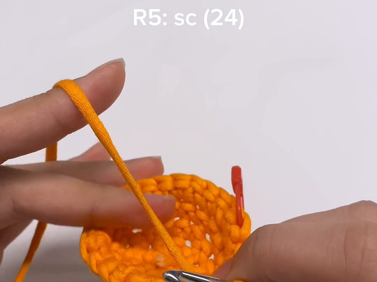 A round of orange single crochet with the pattern line R5: sc (24) shown above it