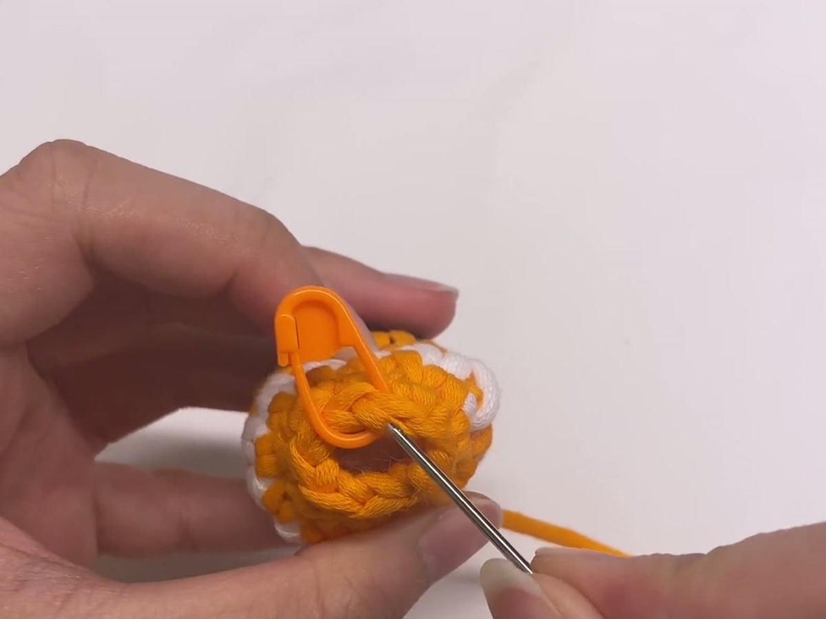 Finishing an amigurumi piece with an invisible fasten off, the yarn needle going back into the stitch marked with a stitch marker