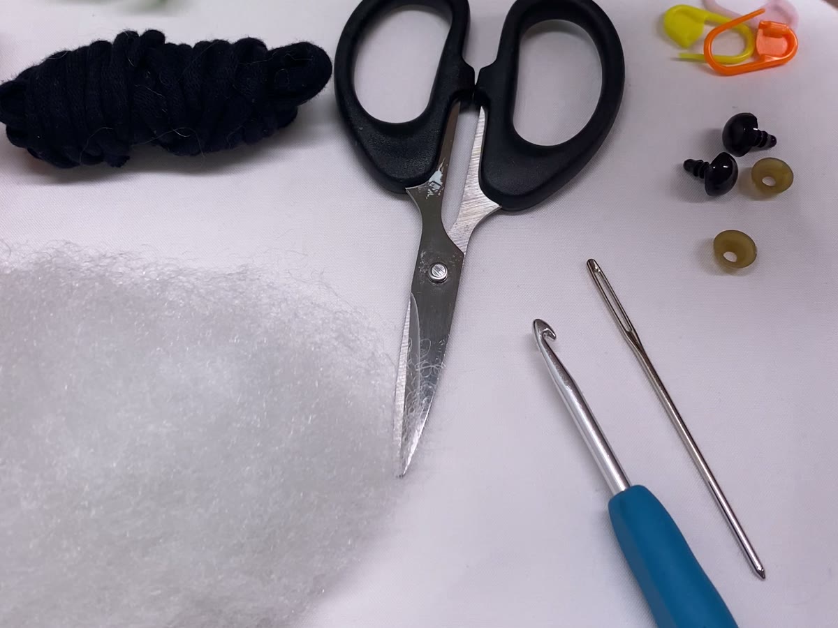 Crochet materials laid out: yarn, hook, blunt needle, scissors, stuffing, safety eyes and stitch markers
