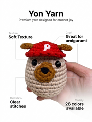 Yon Crochet Pug the Dog. Crocheted animal toy with a red cap held by a hand, featuring Yon Yarn branding and product features.